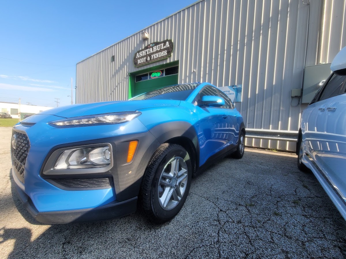 A freshly finished blue Hyundai Kona parked outside Ashtabula Body & Fender's shop, with the OPEN sign lit in the window